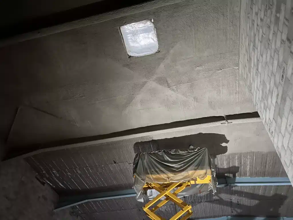 protection-incendie-enduit-pateux Application d’enduit pâteux projeté sur un plafond en béton dans le cadre d’une solution de protection incendie pour bâtiment industriel.