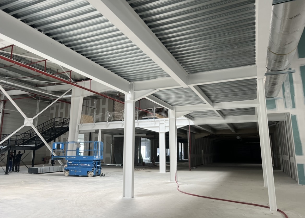 Vaste intérieur de chantier commercial en rénovation. Structure métallique blanche, mezzanine, plafond en tôle ondulée et plate-forme élévatrice bleue.