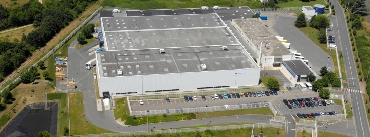 Complexe industriel et logistique moderne vu du ciel. Grand bâtiment d'entrepôt, quais de chargement pour camions, et parkings employés.